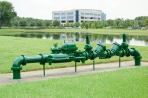 Bright green water pipelines and valves, showcasing plumbing infrastructure by Green Hills Plumbing near calm water.