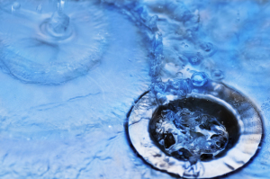 Flowing water in a kitchen sink drain, emphasizing the importance of safe plumbing solutions over chemical drain cleaners.