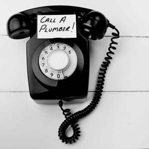 Black rotary phone with a note saying "Call a Plumber," emphasizing the importance of professional plumbing services for preventing burst pipes.