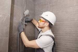 Plumber installing a modern showerhead in a bathroom, emphasizing professional plumbing skills for bathroom remodeling.