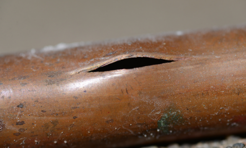 Close-up of a damaged copper pipe with a visible split, illustrating potential plumbing emergencies like burst pipes during the holiday season.