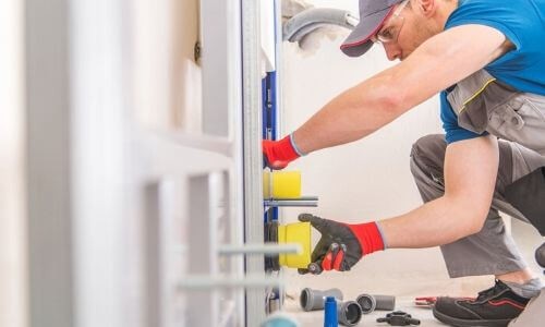 A technician in gray overalls installing plumbing components with tools, representing Green Hills Plumbing services.