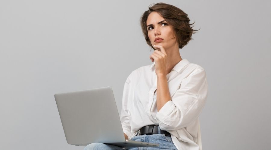 Woman with laptop, wearing white shirt and jeans, focused on plumbing tips for land and property management.