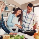 Three people cooking in a bright kitchen with utensils and vegetables, highlighting plumbing tips by Green Hills Plumbing.