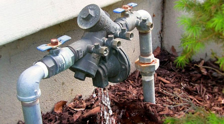 Outdoor plumbing setup showing a water faucet, gray metal pipes, and brass valve handles at Green Hills Plumbing service.
