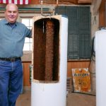 Man beside two water heaters, one cut open to show honeycomb structure, illustrating plumbing maintenance needs.