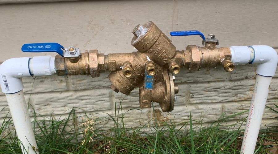 Plumbing valve assembly with blue handles and brass fittings in an outdoor setting, part of Green Hills Plumbing services.